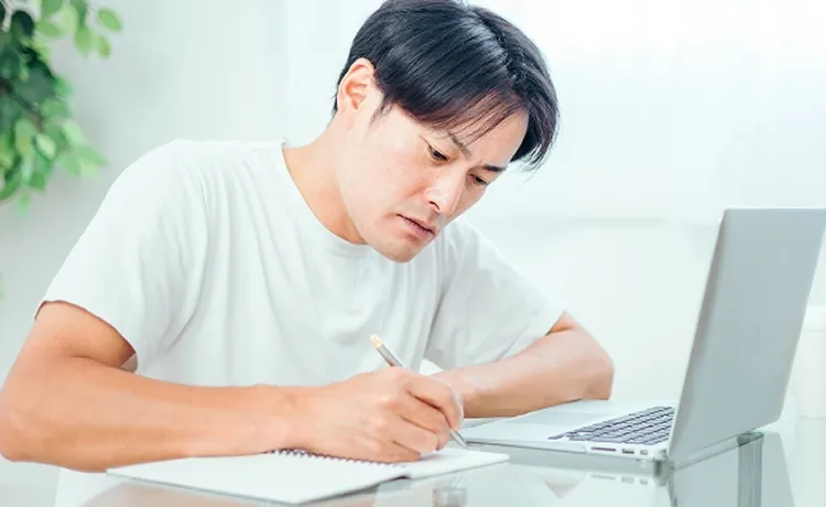 パソコンの前でメモしている男性の写真